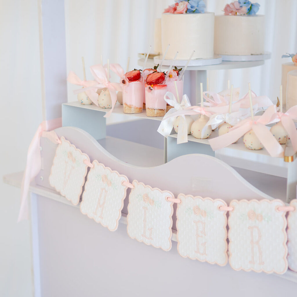 Elegant baby shower dessert table with mini cakes, cake pops, floral arrangements, and blush décor.